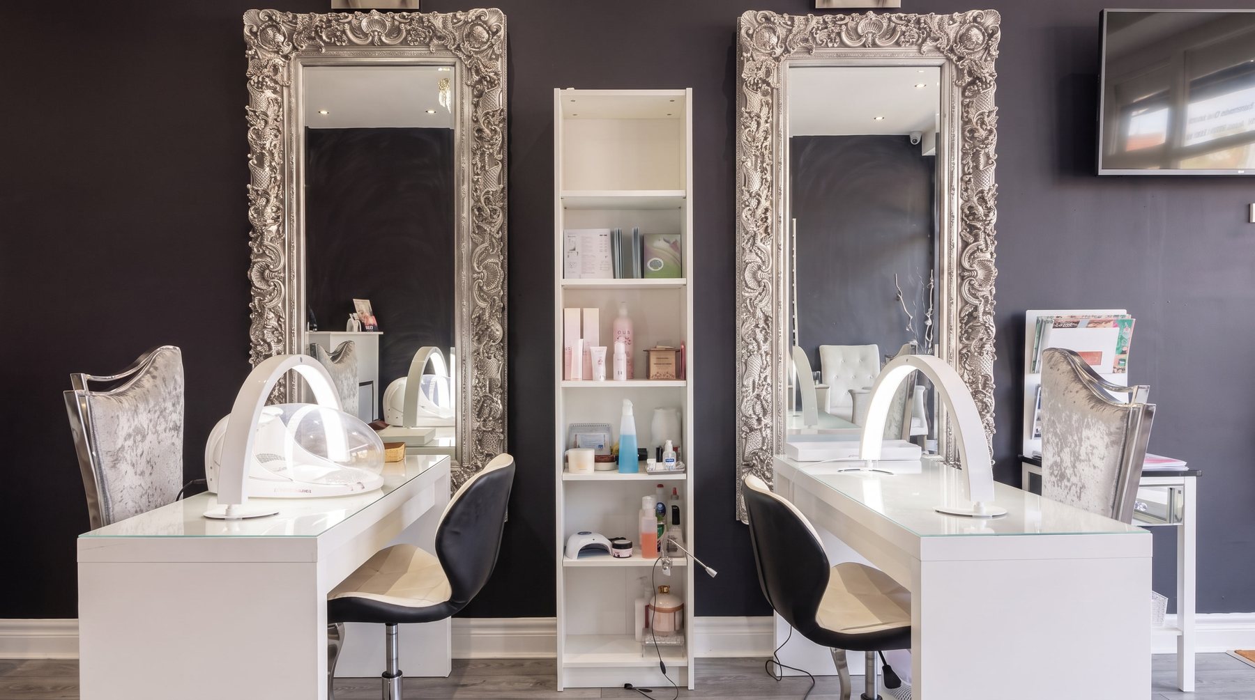 The nail desks and velvet chairs under the tall silver mirrors