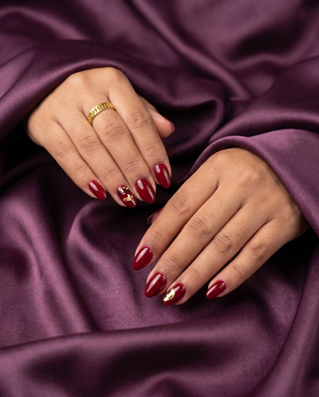 Deep red almond nails with a gold foil accent